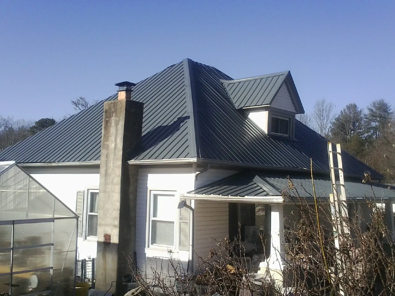 Dark blue standing seam metal roof on a white farmhouse with dormer — Slate & Tile Roof Repair by Roofing Brothers in Meade