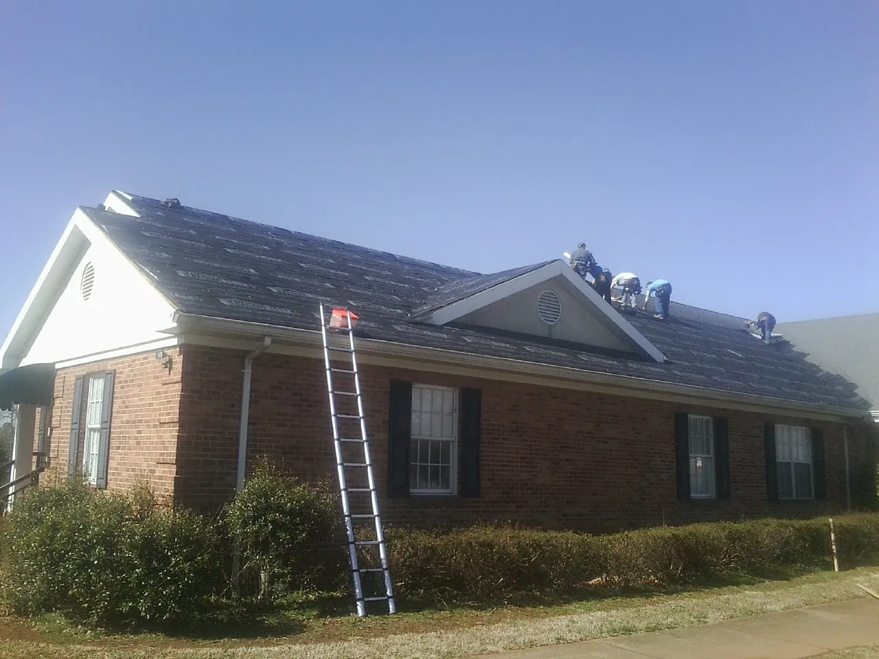 Crew tearing shingles off a brick ranch roof with a ladder set — Emergency Roof Repair work by our crew in Meade