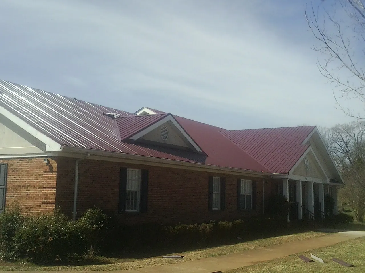 Red metal roof with gabled entries on a long brick building, from a Hail Damage Roof Repair job in Meade