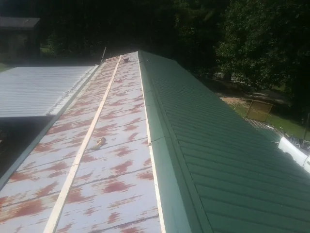 Old rusted panels beside newly installed green metal roofing — Wind Damage Roof Repair by Roofing Brothers in Meade