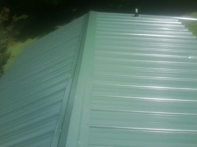 New green metal panels meeting at the ridge of a roof — Flat Roof Repair work by our crew in Meade