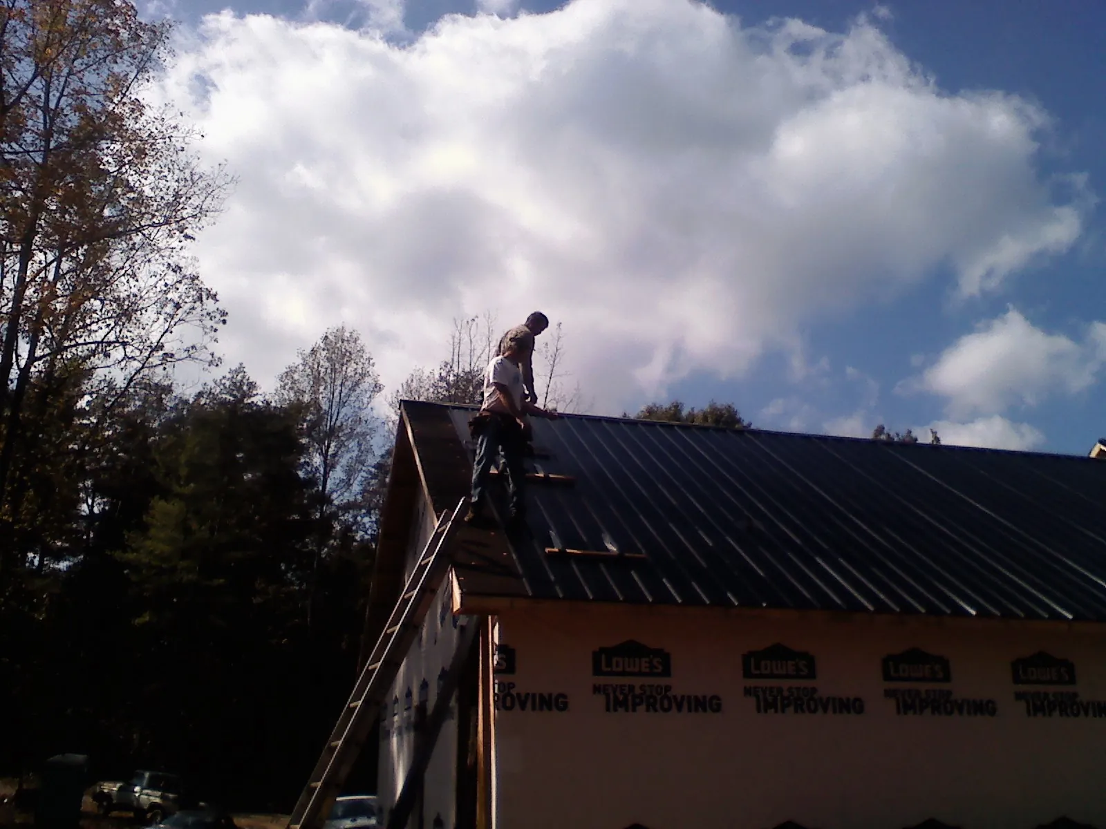 Roofer fastening dark metal panels high against a cloudy sky, from a Roof Inspection job in Meade