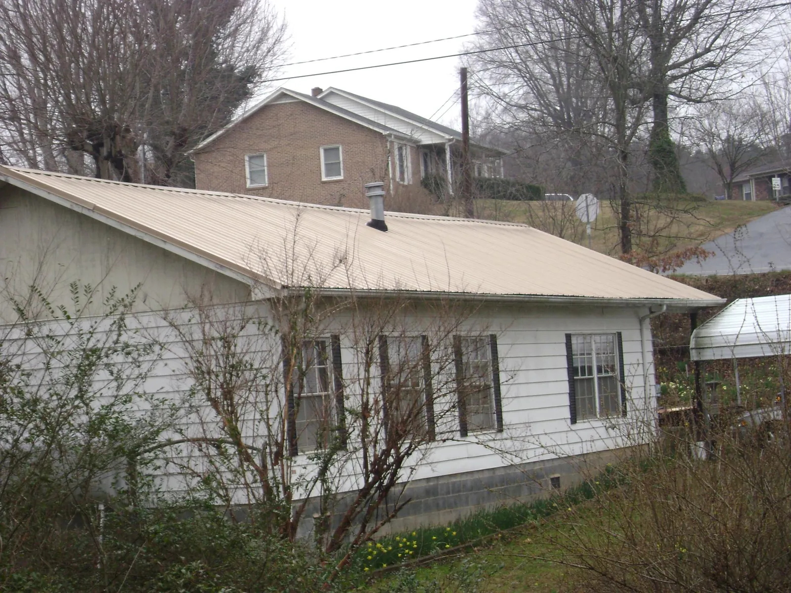 Tan metal roof on a white sided house set into a hillside — Commercial Roofing by Roofing Brothers in Meade