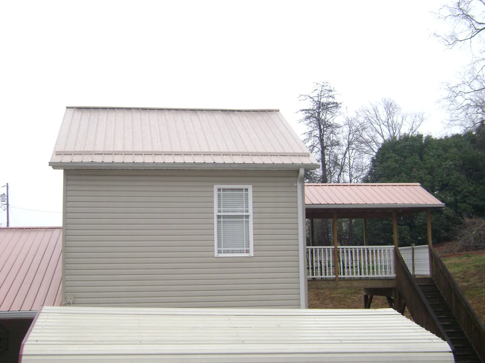 Tan metal roofs on a two story addition and attached porch, from a Roof Replacement job in Meade